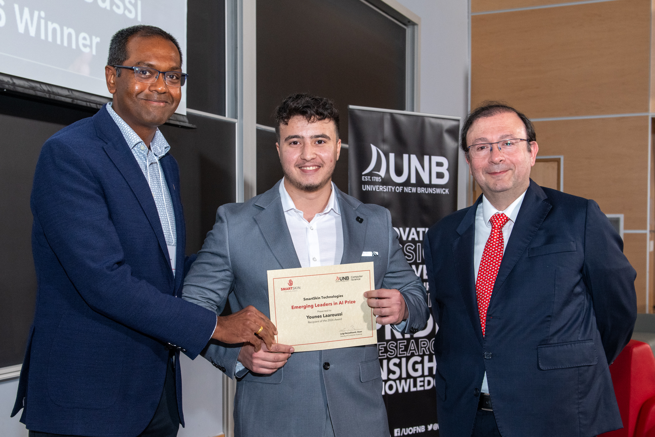 Younes Laaroussi holding the SmartSkin Emerging Leaders in AI Prize certificate alongside two presenters at the University of New Brunswick.